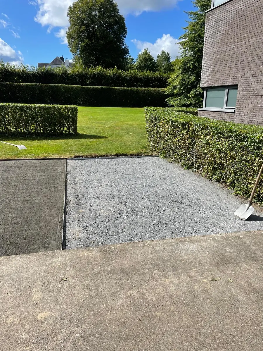 Allée en gravier bordée d’une haie basse et d’une bordure en béton.