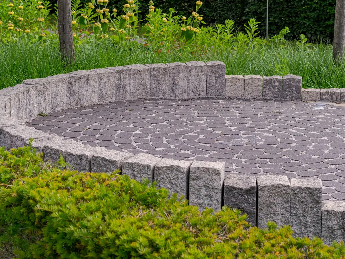 Terrasse pavée circulaire bordée d'un muret et de plantations.